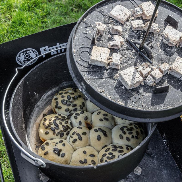 Brötchen in einem Dutchoven gebacken bei dem der Deckel mit heißen Kohlen mit einem Deckelheber weggehoben wird